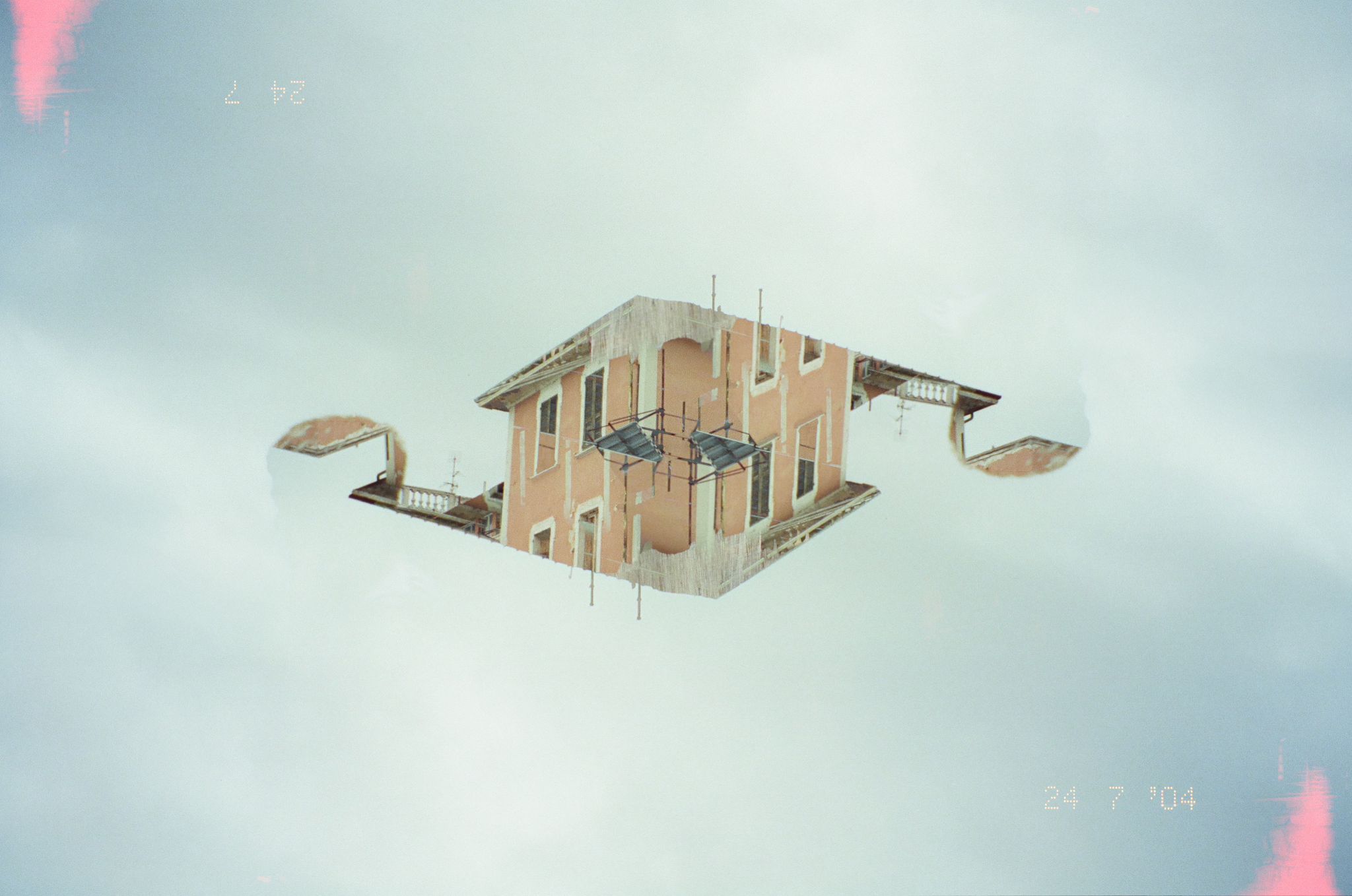Surreal bearbeitetes Foto eines Gebäudes, das gespiegelt in einem wolkigen Himmel schwebt, mit Vintage-Fotofilter und Datumsstempel '24 7 '04'.